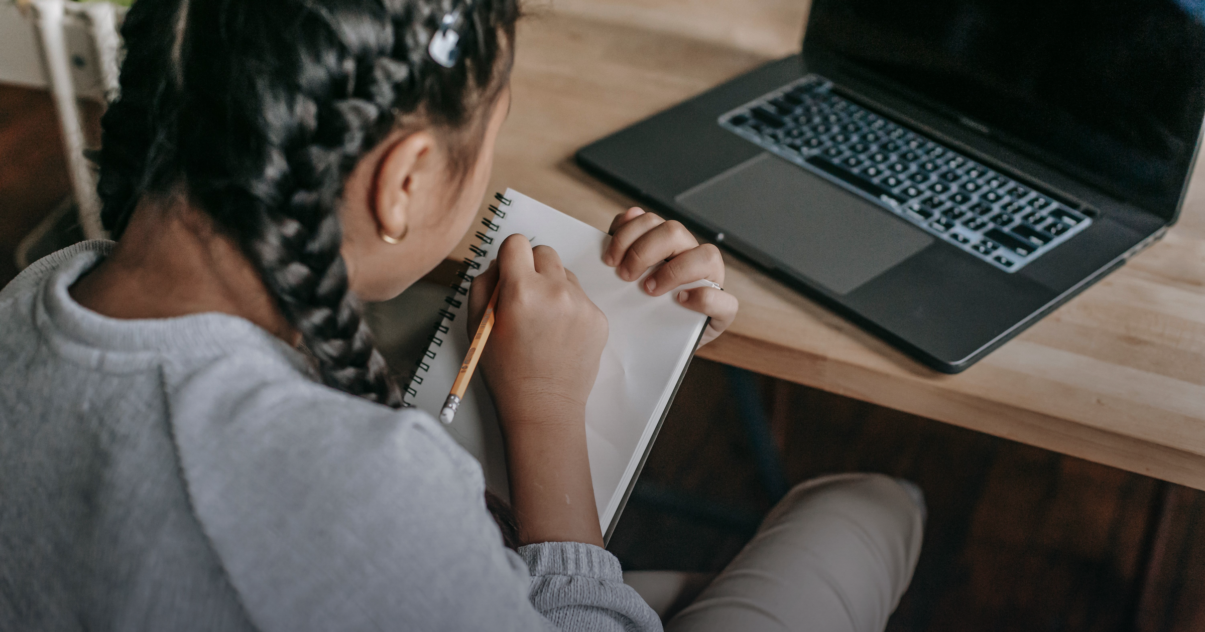 Student writing in a notepad beside an open laptop
