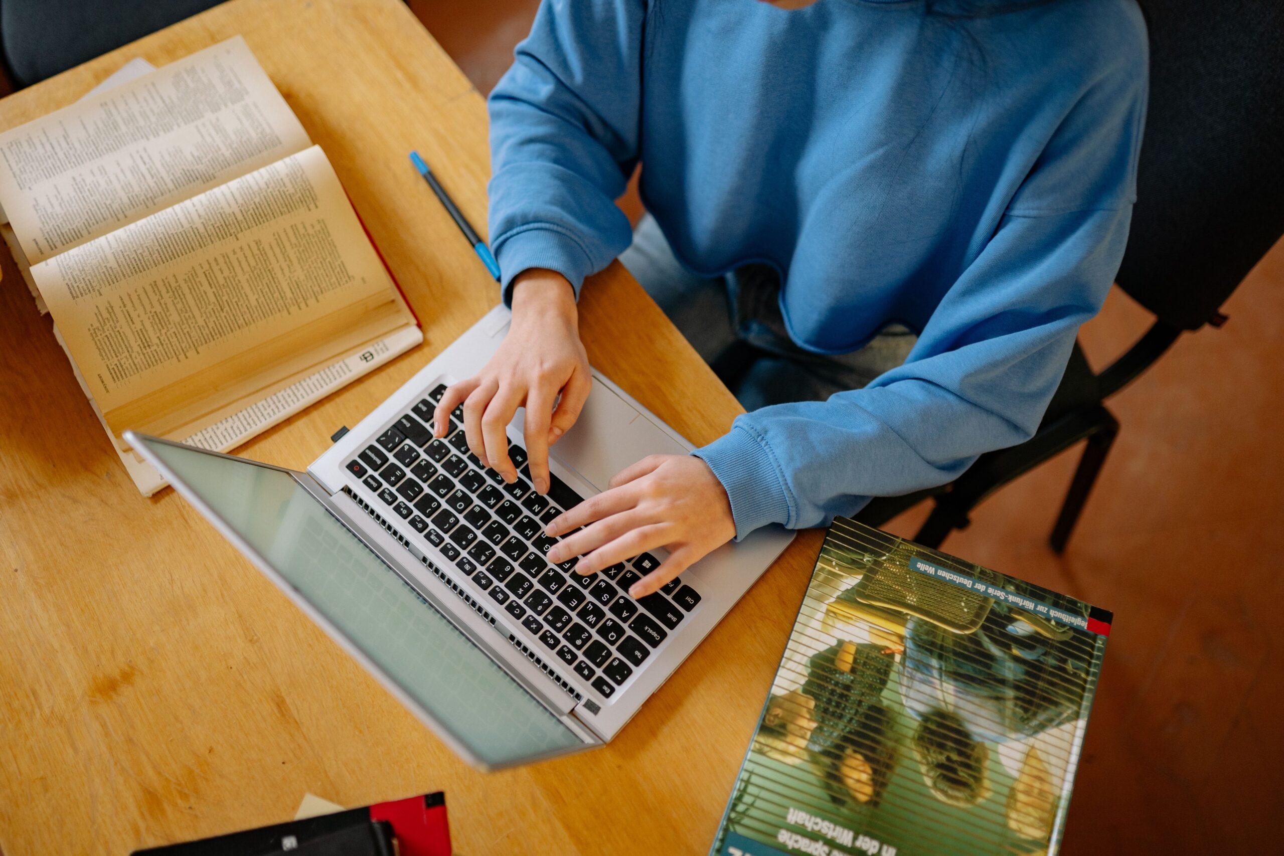 Overhead view of hands typing on a laptop beside an open textbook while studying for the AWS Certified AI Practitioner exam
