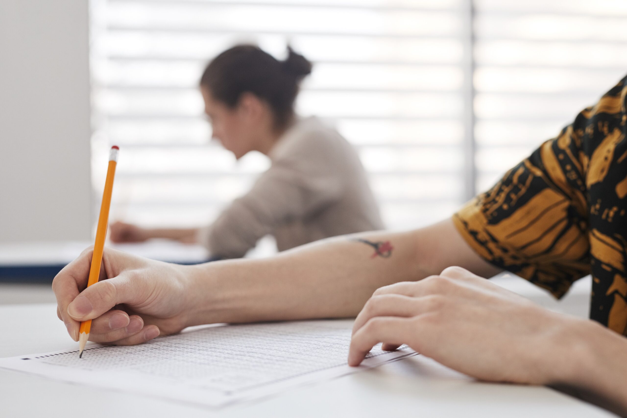 Close-up of a student's hand filling in a multiple-choice bubble answer sheet with a pencil during an exam