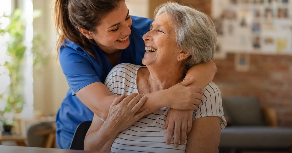 A caregiver embracing and supporting a smiling elderly woman