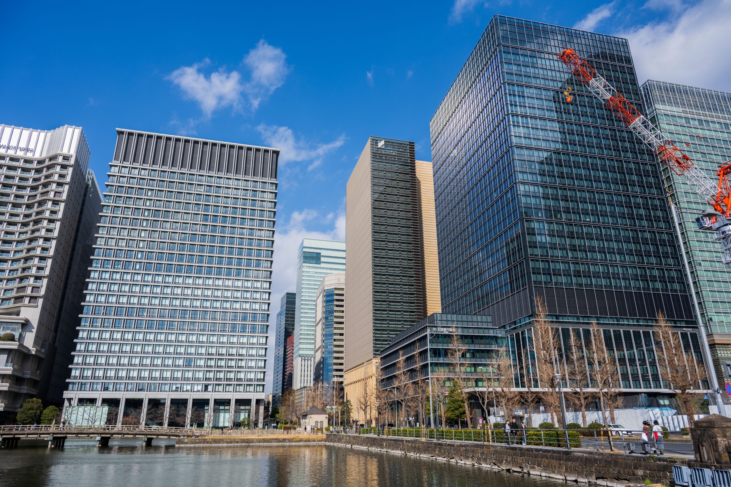 Modern high-rise office towers in Tokyo's business district reflected in water under a blue sky