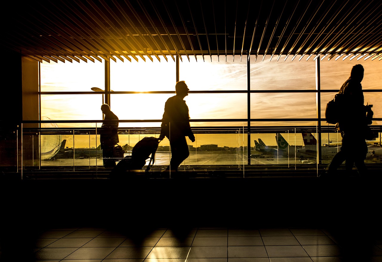 Travelers with luggage silhouetted against airport windows at sunset before departure