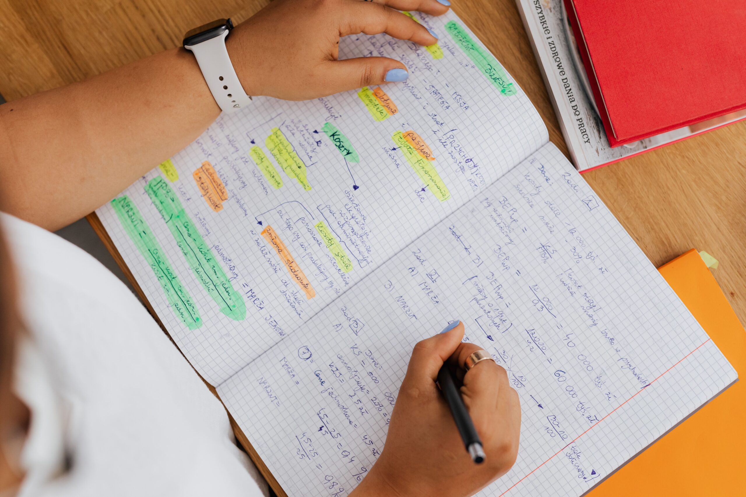 Overhead view of hands writing color-highlighted Japanese study notes in a grid notebook