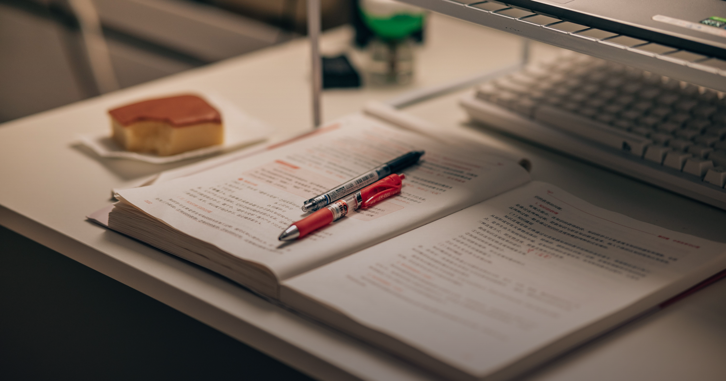 Open study book with notes, pens, keyboard and coffee on a desk