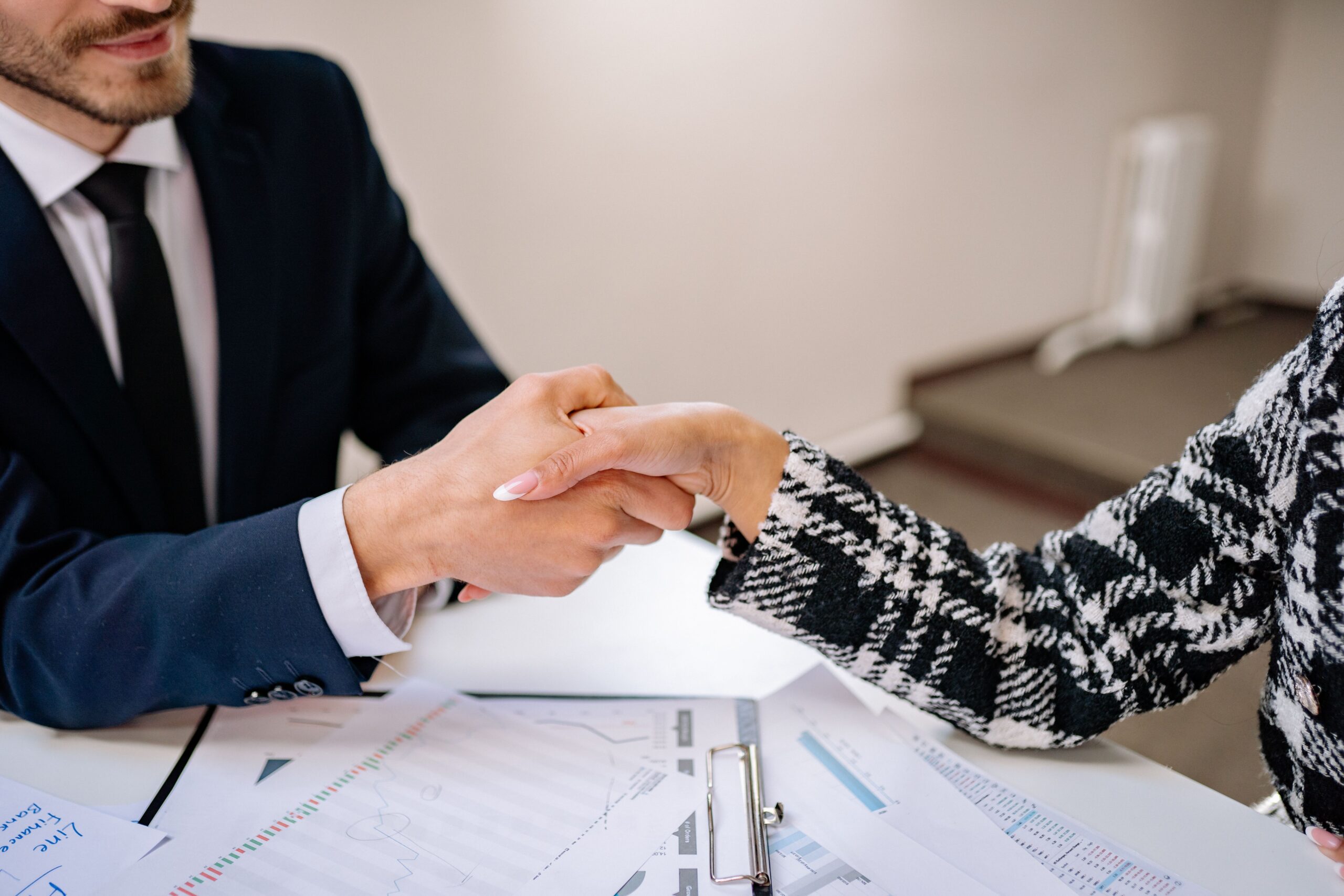 Two people shaking hands over documents in a modern office, representing a job introduction