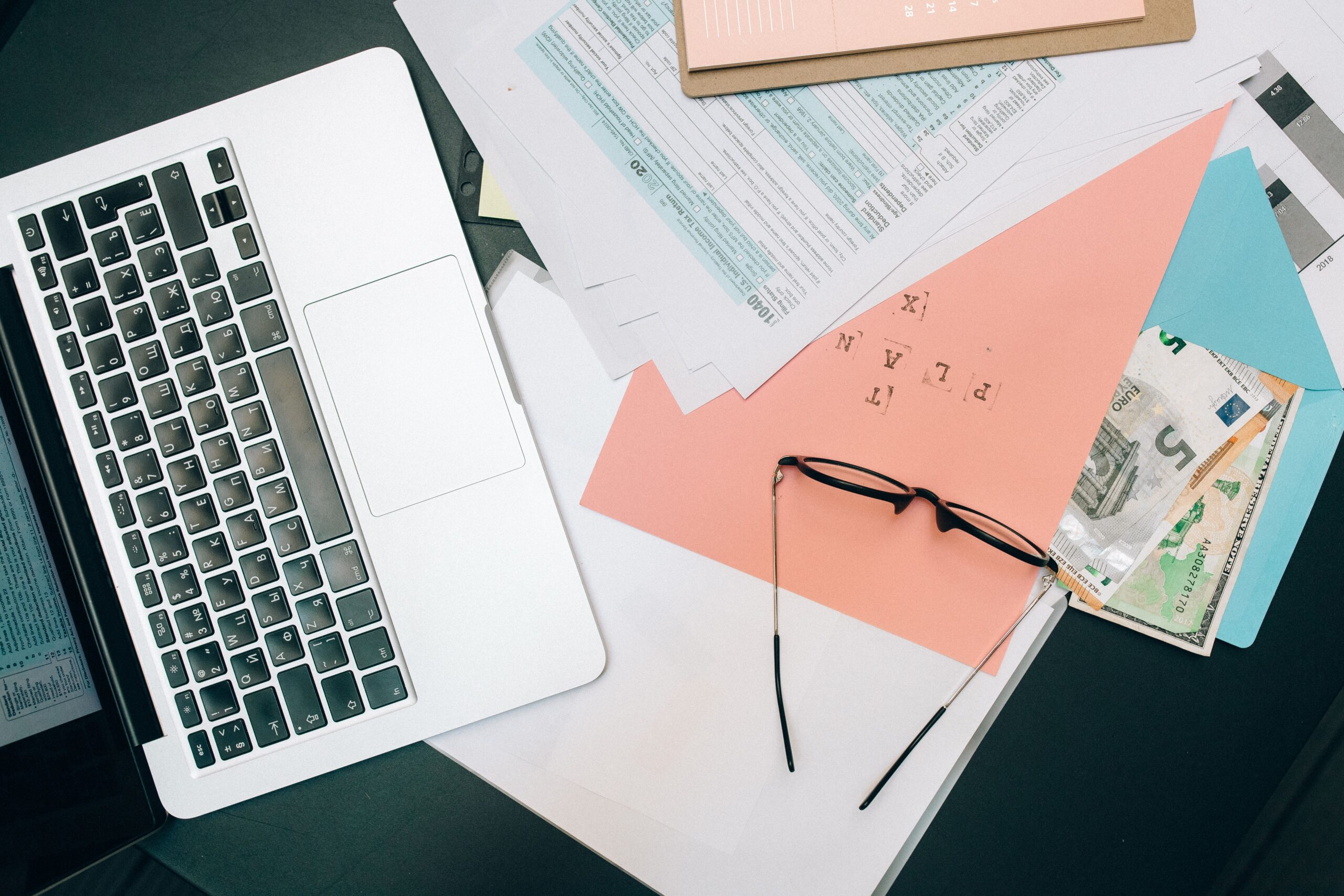 Laptop, financial documents, eyeglasses and cash on a desk representing investment planning in Japan