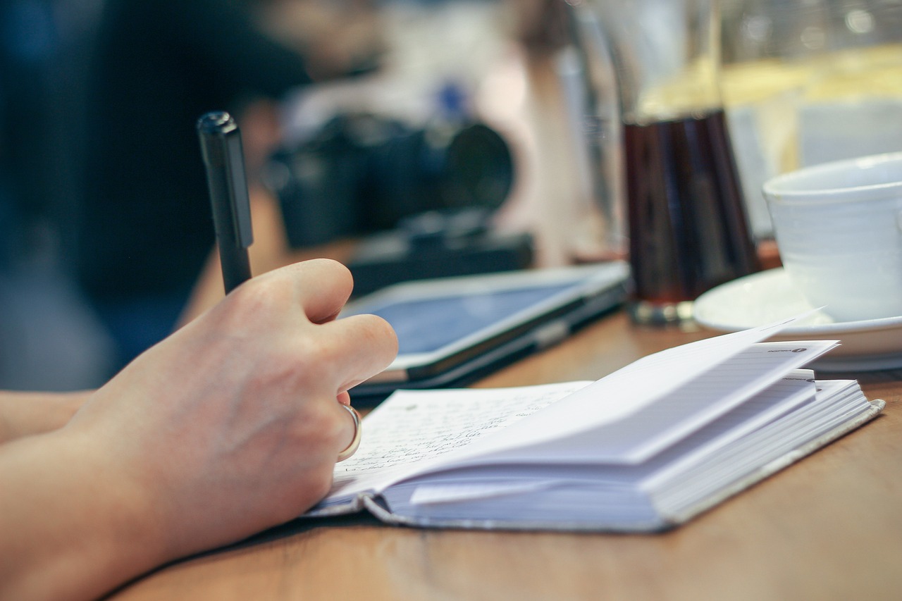Hand writing notes in an open journal beside a coffee cup
