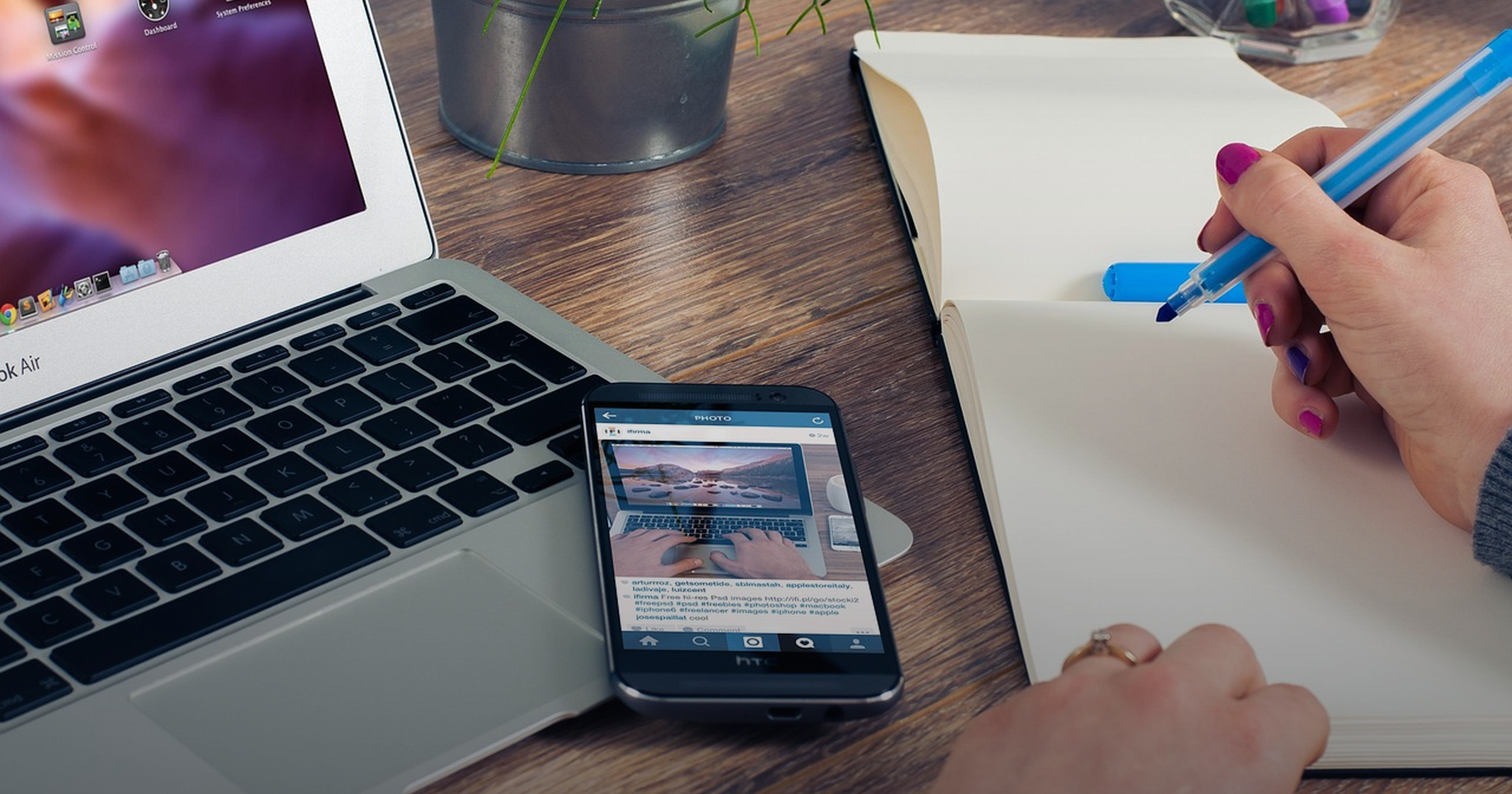 Overhead desk flat-lay with a laptop, phone and a hand writing in a notebook