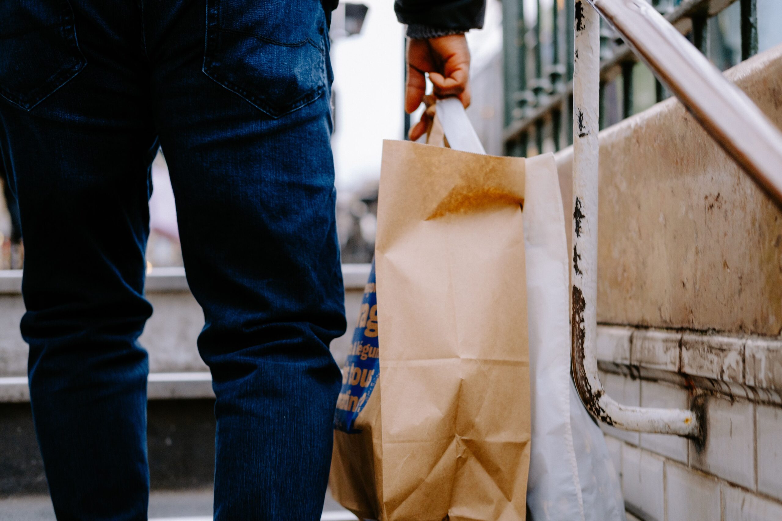 Person carrying brown paper retail shopping bags up city steps after a shopping trip